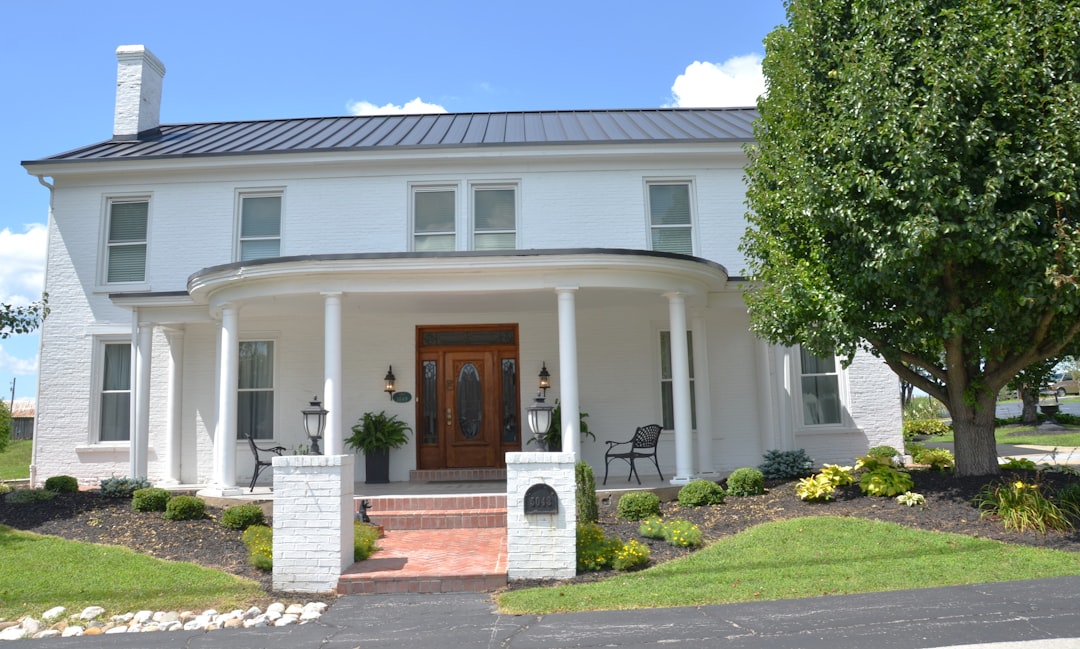 A white brick house with a curved porch and dark metal roof