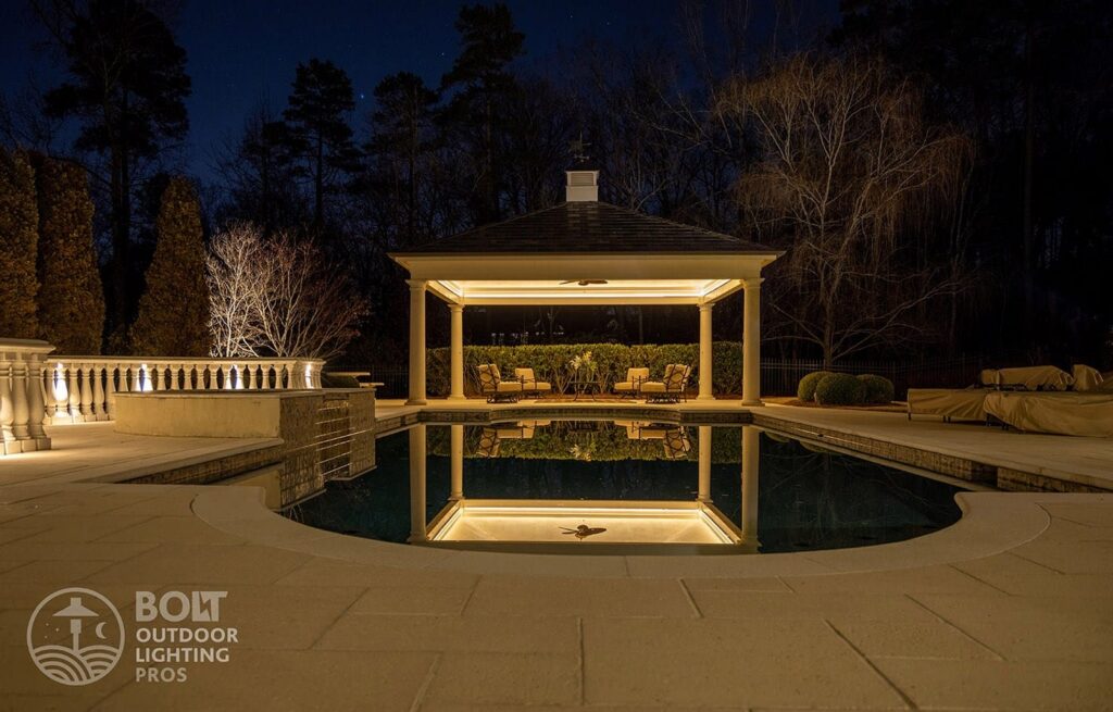 Custom pool and pavilion lighting creating warm reflections across an outdoor living space